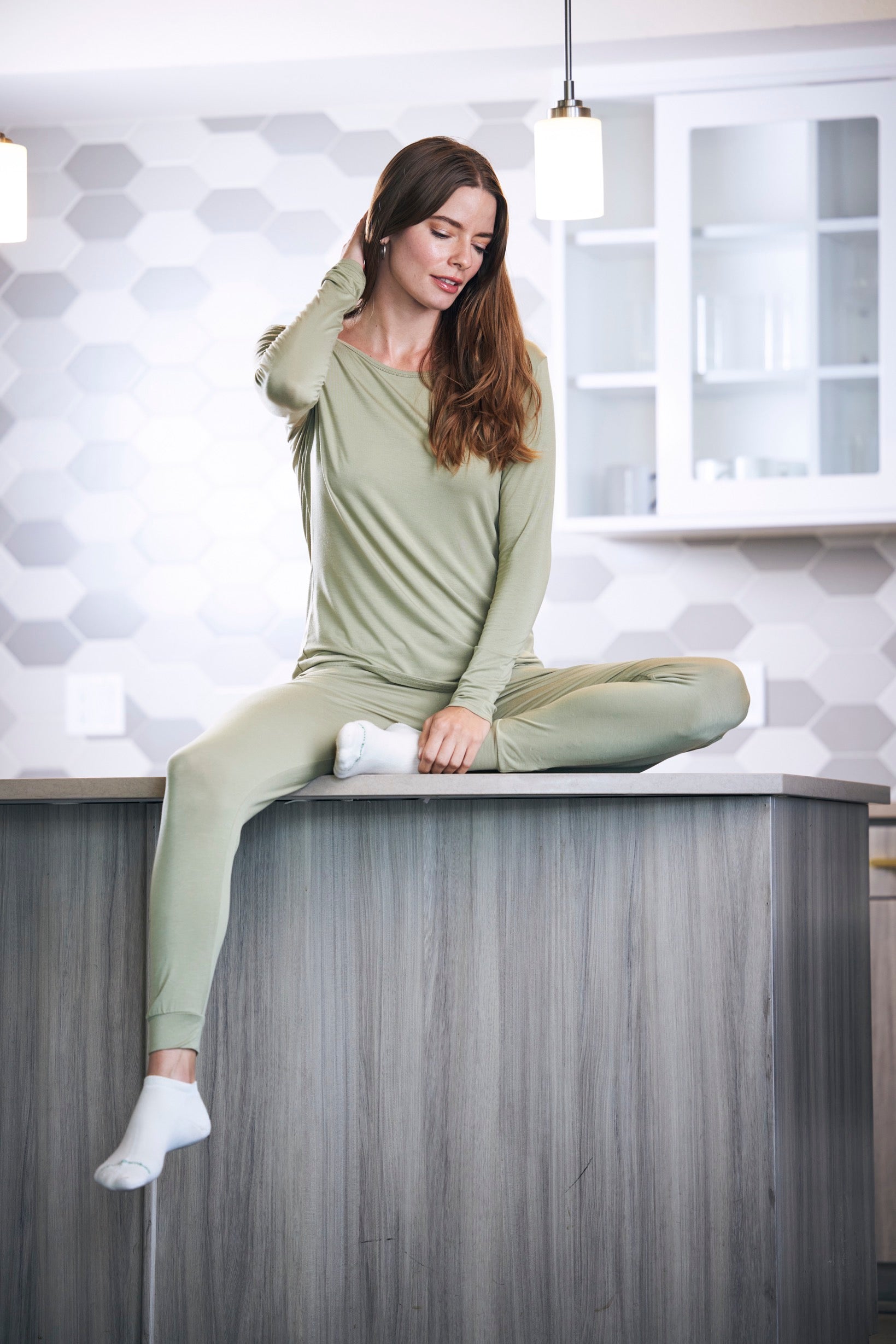 Woman in green pajamas sitting on a kitchen counter with a geometric wall pattern in the background