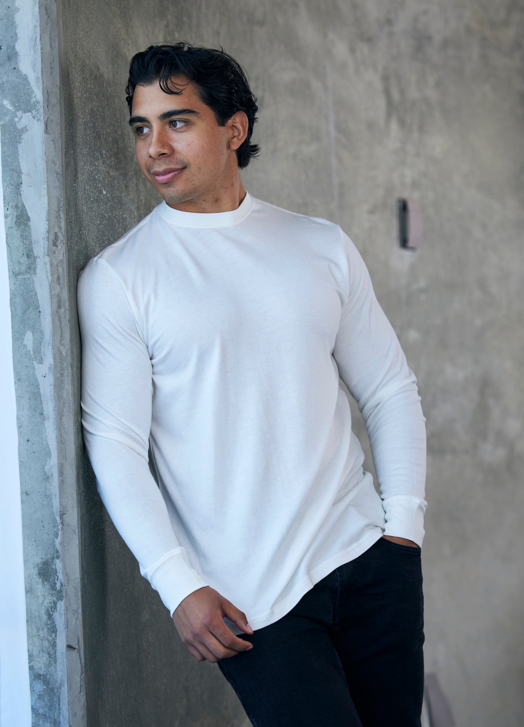 Man wearing a white long-sleeve shirt against a textured wall.