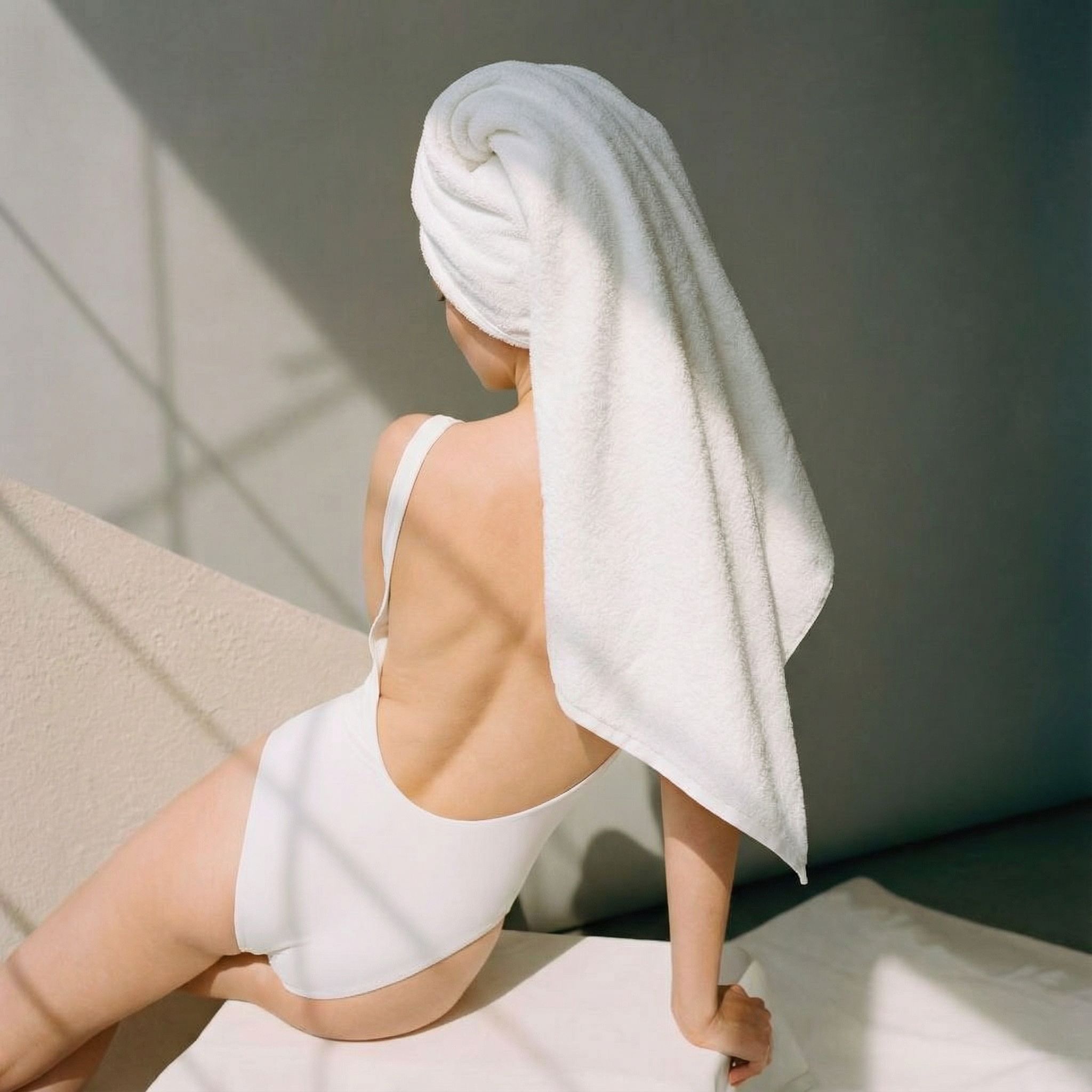 Person wrapped in a white towel sitting on a light-colored surface with a neutral background