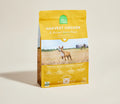 A bag of Open Farm Harvest Chicken & Ancient Grains Recipe dog food, featuring a bright yellow packaging with a photo of a dog in a field, set against a warm beige background.