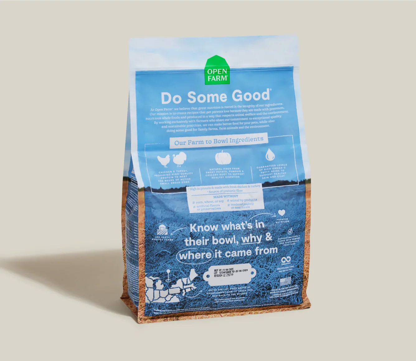 A bag of Open Farm 'Do Some Good' chicken and apple flavored pet food, standing upright on a neutral beige background with a soft shadow to the left.