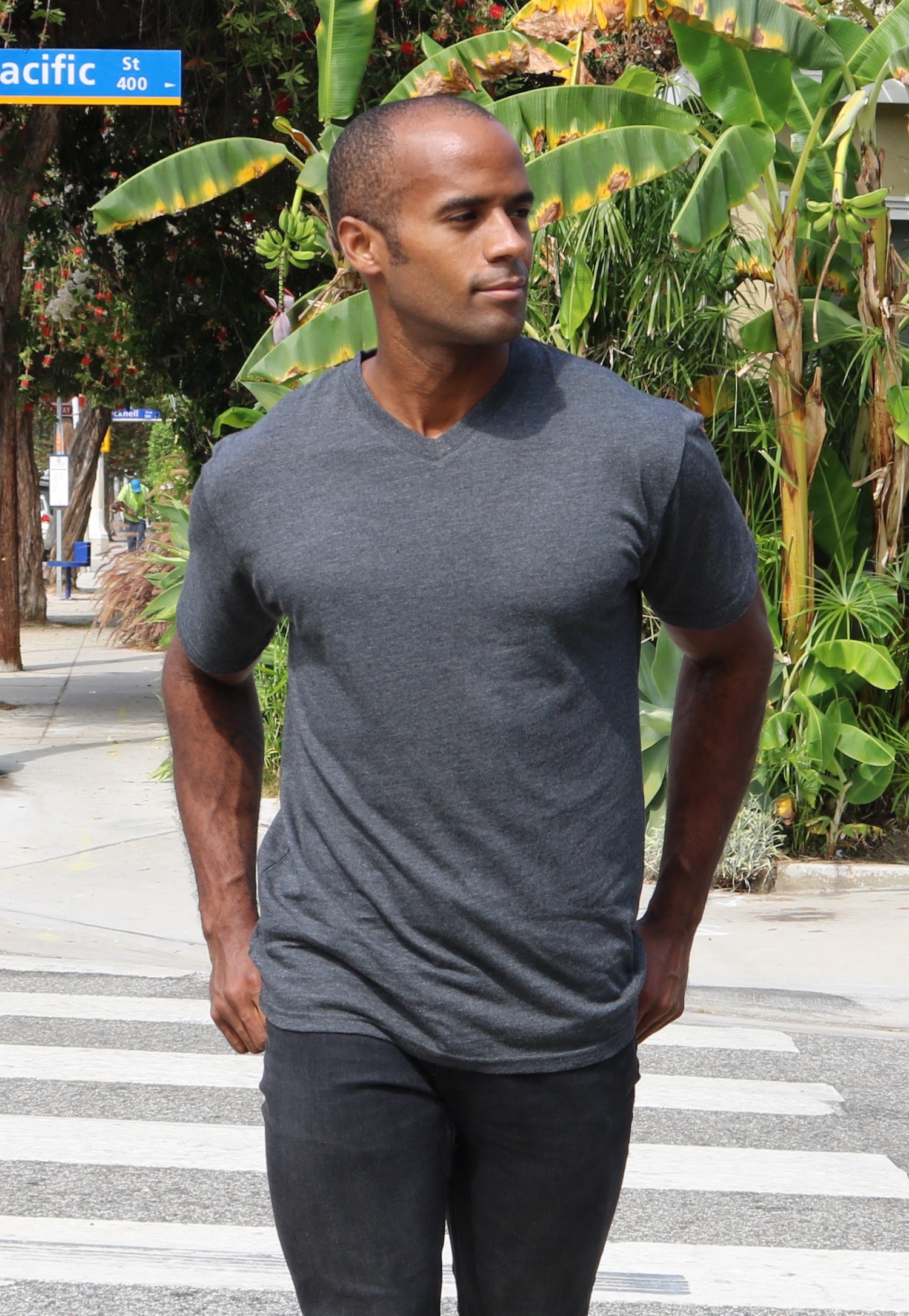 Man in a gray t-shirt walking on a crosswalk with greenery in the background