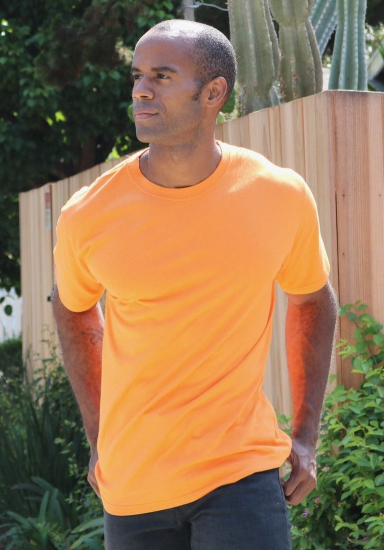 Man wearing an orange t-shirt standing outdoors with greenery in the background
