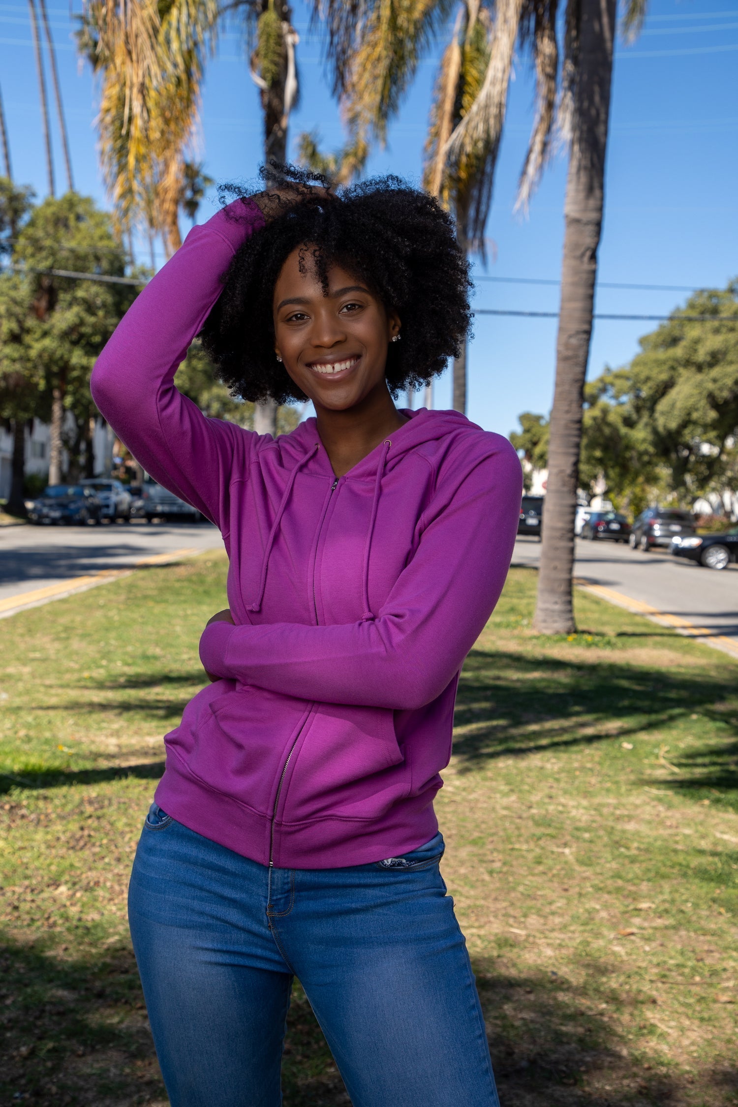 Person wearing a purple hoodie and blue jeans standing outdoors with palm trees in the background